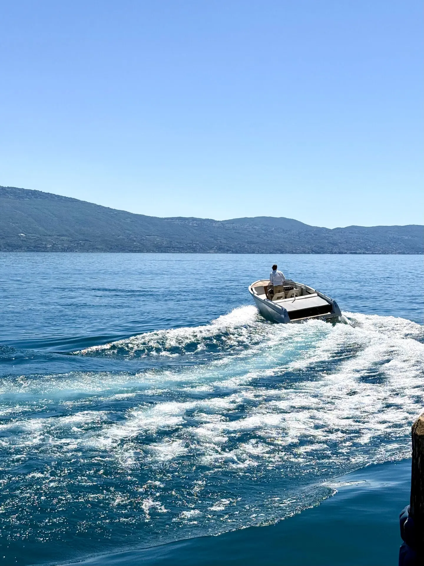 Mitfahrendes Motorboot auf dem Gardasee bei Gargnano mit weißer Heckwelle, klarem Himmel und Bergen im Hintergrund beim SBF-See und Binnen Training.